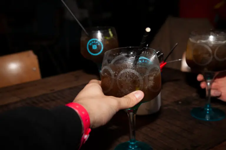 The hand of a man wearing a pink wristband holding a glass of long island ice tea and cheering