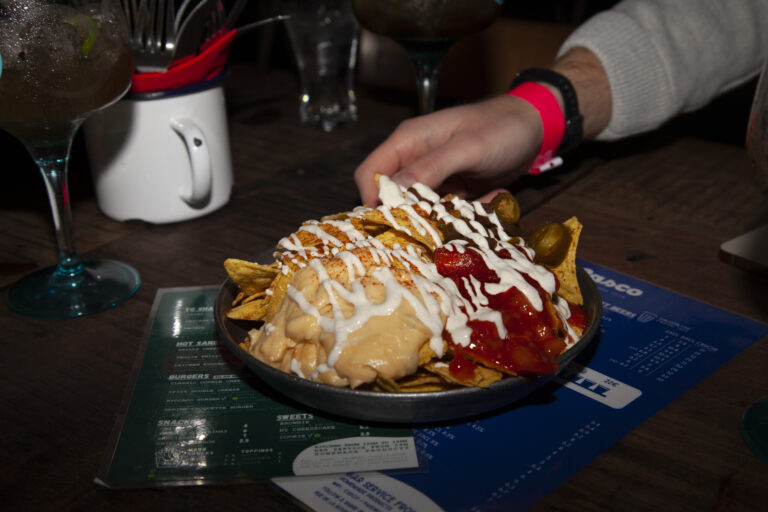 The hand of a man wearing a pink wristband reaching for a plate of nachos